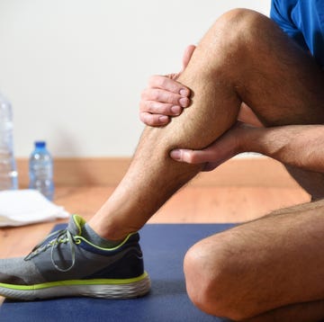 detail of man doing sports with calf pain holding himself with his hand sitting on a mat side view