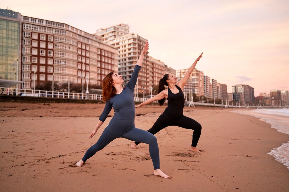 two sportive female friends doing yoga in an urban beach in the morning