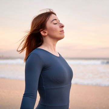 sportive young woman breathing with eyes closed on the beach during sunset