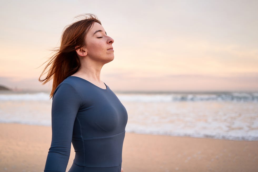 sportive young woman breathing with eyes closed on the beach during sunset