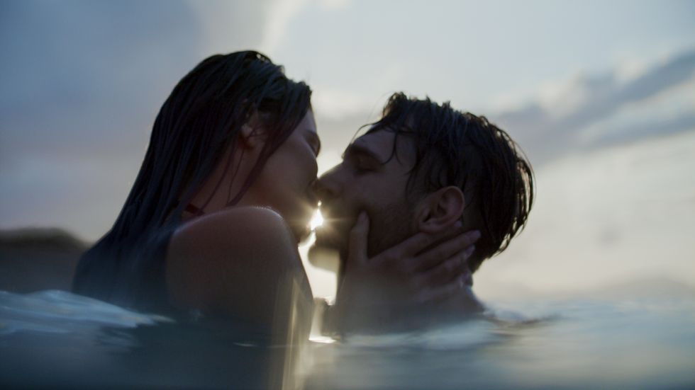 romantic heterosexual couple relaxing in the water at beautiful sunset embracing and playing in the sea