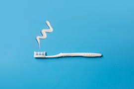 close up view of one flat lay white toothbrush and tooth paste on blue background