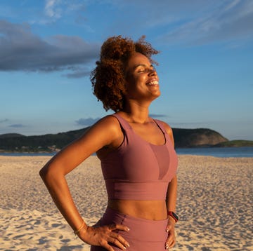 vrouw in sportkleding geniet met ogen dicht van het zonnetje op het strand