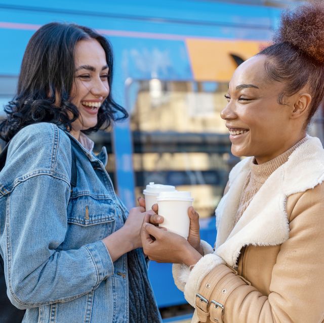 two women in a denim jacket is talking to each other , drinking coffee and waiting for a tram at the stop lifestyle photo