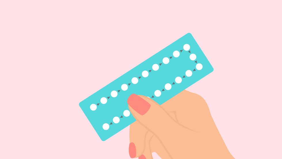 female hand holding birth control pills on pink background
