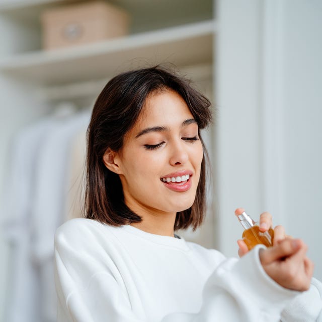 Toothy smiling woman spraying and testing perfume oil water on her wrist seductive, satisfied brunette woman applying spraying perfume bottle as essential oil on the wrist