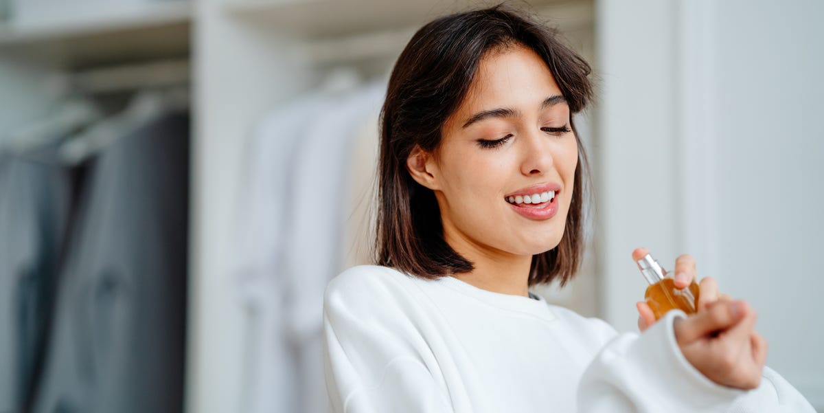 Toothy smiling woman spraying and testing perfume oil water on her wrist seductive, satisfied brunette woman applying spraying perfume bottle as essential oil on the wrist
