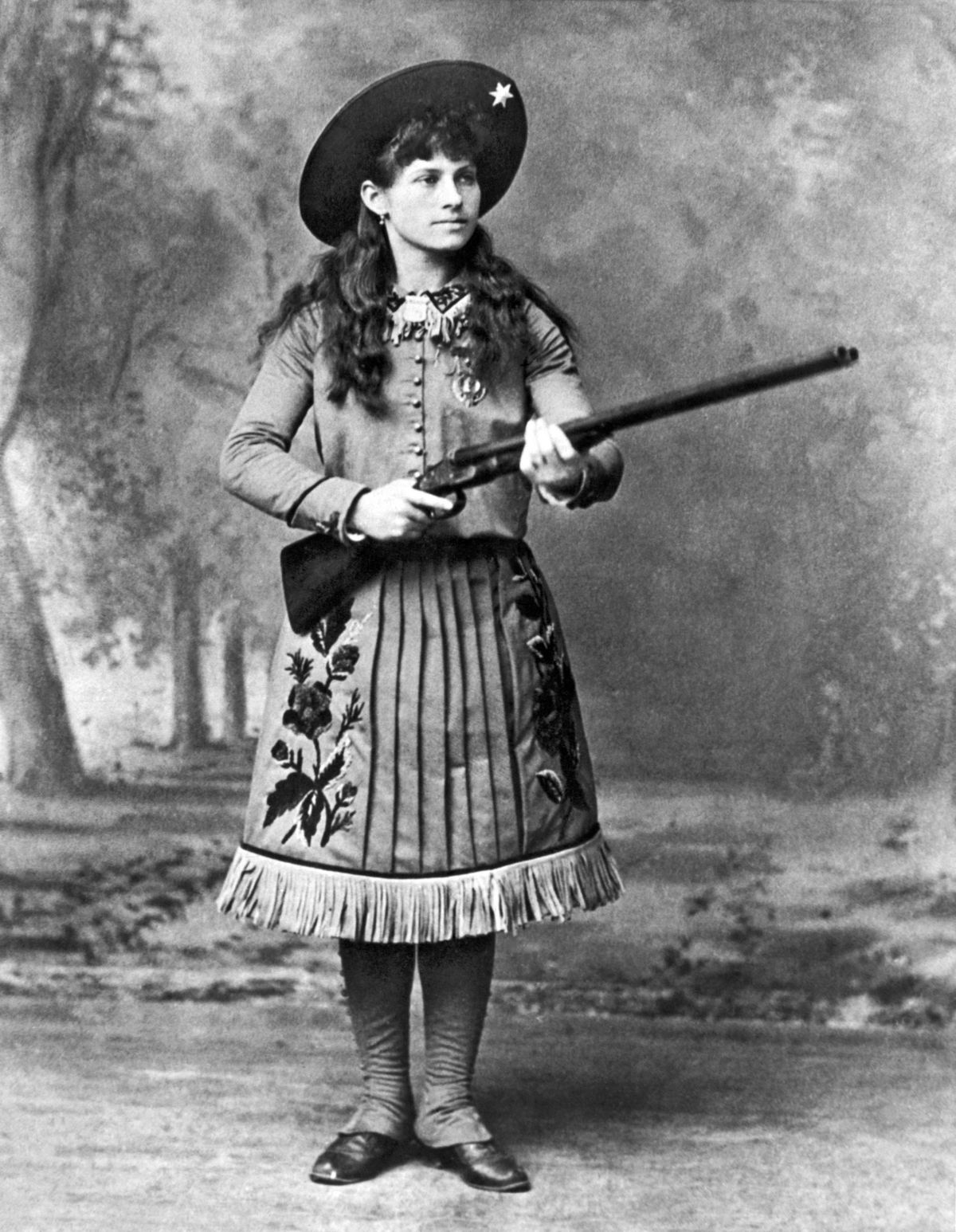 Op dit portret uit het midden van de jaren 1880 houdt scherpschutter Annie Oakley een jachtgeweer vast De meer dan levensgrote legende die de hoofdrol speelde in Buffalo Bills Wild West Show was een inspiratiebron voor tvprogrammas films en musicals En voor vele tegenstrijdige verslagen over haar leven