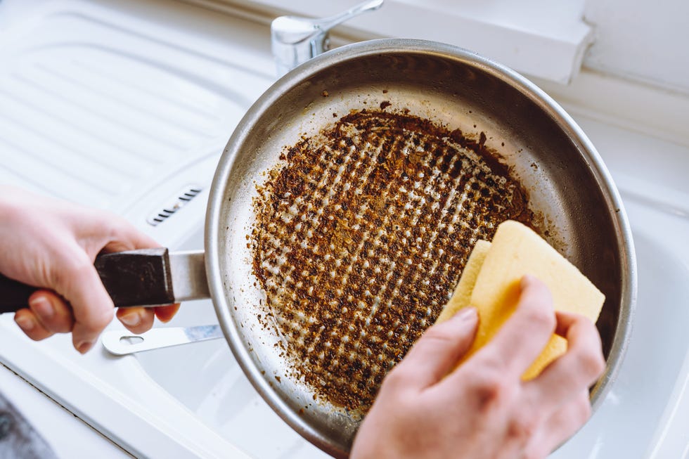 womans hand washes burnt greasy frying pan with kitchen washcloth in sink. dirty dishes with burnt food, household chores, washing dishes