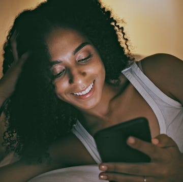 Night, black woman and smartphone for social media, communication and texting while in bed, smile or chatting. Dark, African American female or lady in bedroom with cellphone to search or read online goodnight texts