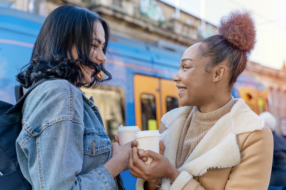 two women in a denim jacket is talking to each other , drinking coffee and waiting for a tram at the stop lifestyle photo