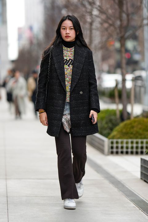 new york, new york february 12 a guest wears a black wool turtleneck pullover, a multicolored braided wool pullover, a black tweed coat, a pale blue denim belt, a beige with black and red checkered print pattern short skirt, dark brown flared pants, white shiny leather sneakers from new balance, outside ulla johnson, during new york fashion week, on february 12, 2023 in new york city photo by edward berthelotgetty images