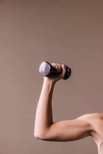 a cropped photo of an unrecognizable caucasian athlete holding a weight while doing her daily workout for her arm muscles studio shot, pink background, copy paste