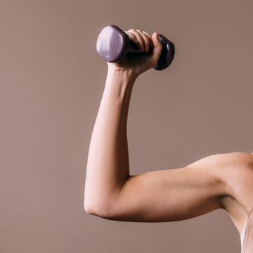 An Unrecognizable Woman Exercising With A Dumbbell a cropped photo of an unrecognizable caucasian athlete holding a weight while doing her daily workout for her arm muscles studio shot, pink background, copy paste