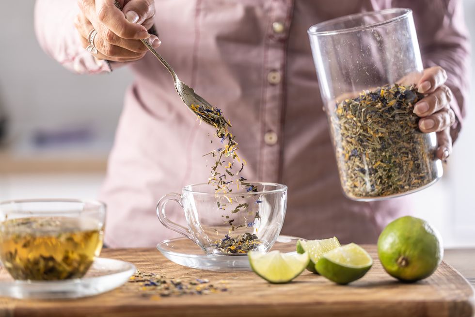 a woman pours dried tea leaves into a glass cup
