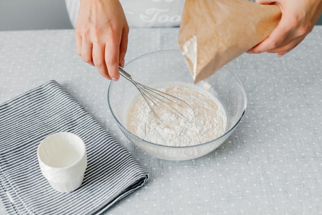 a woman pours gluten free flour into a glass bowl. the process of preparing healthy pastries. gluten free diet