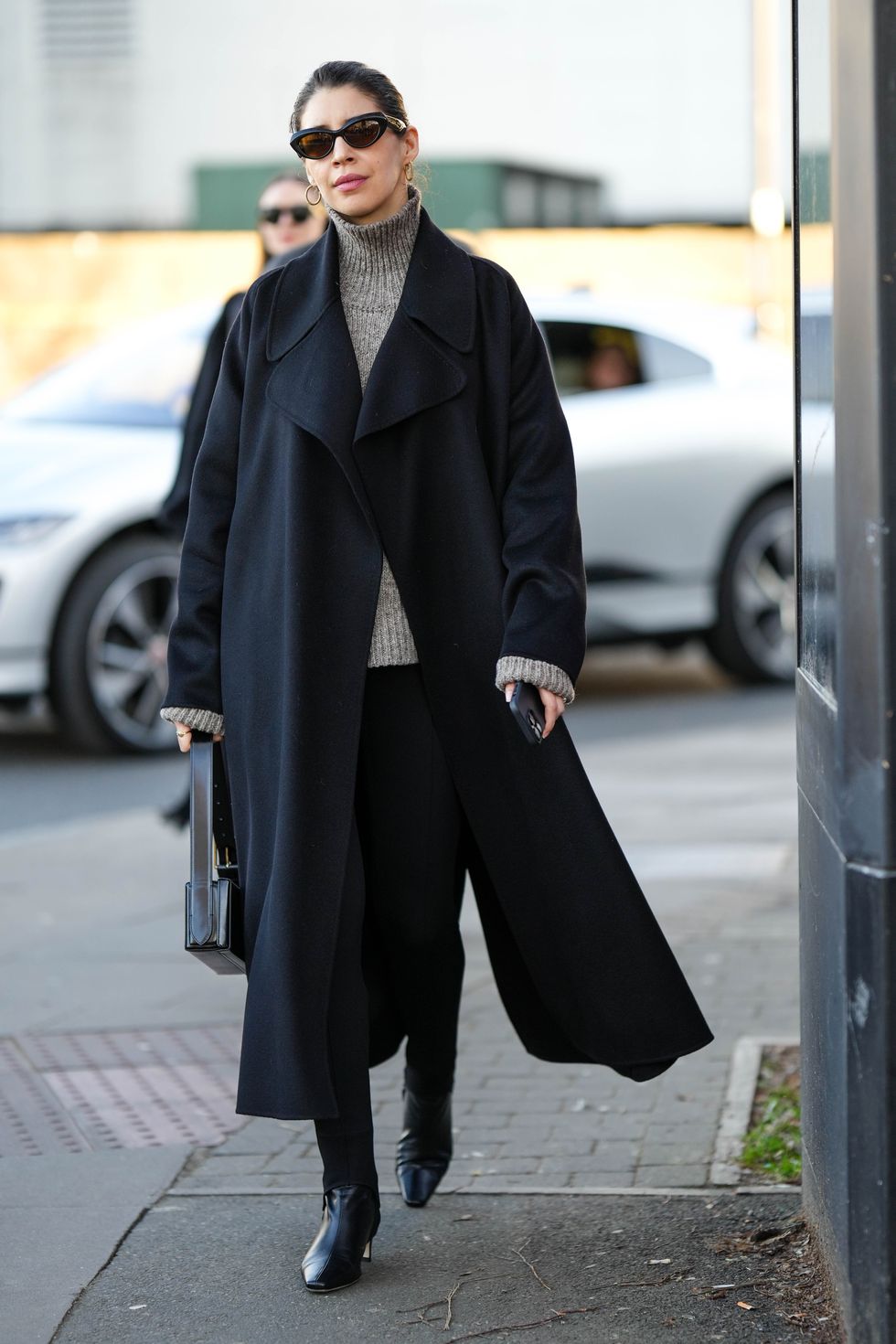 london, england february 19 a guest wears black sunglasses, gold earrings, a gray wool ribbed turtleneck pullover, a black long coat, black legging pants, a black shiny leather handbag, black shiny leather heels ankle shoes , outside nensi dojaka, during london fashion week february 2023 on february 19, 2023 in london, england photo by edward berthelotgetty images
