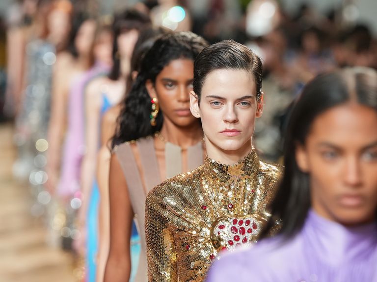 models walking in a line at the paco rabanne fall 2023 show in paris, with the camera focusing on one woman with a proud expression in a gold high necked dress