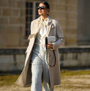 paris, france march 02 julia haghjoo wears black sunglasses, silver large pearl earrings, a white latte silk knot neck blouse, a beige long wool coat, a white embroidered logo pattern and black shiny leather borders handbag from givenchy, white braided tweed wide legs pants, black shiny leather heels ankle shoes , outside givenchy, during paris fashion week womenswear fall winter 2023 2024 on march 02, 2023 in paris, france photo by edward berthelotgetty images