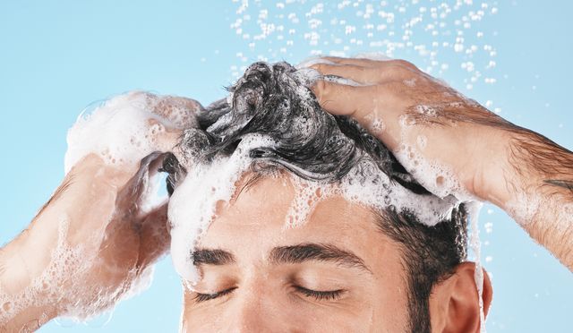 face, water splash and shampoo shower of man in studio isolated on a blue background water drops, hair care and male model washing, bathing or cleaning for healthy skin, wellness or skincare hygiene