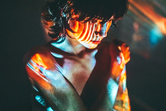 a person is embracing themselves with colorful light projections on their skin