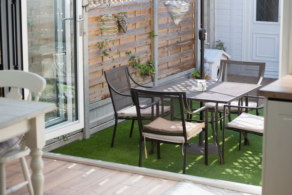 looking through bi fold patio doors into the back gardens with metal table and chairs on fake grass