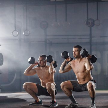 athletic men exercising strength with dumbbells in a squat position in a gym copy space