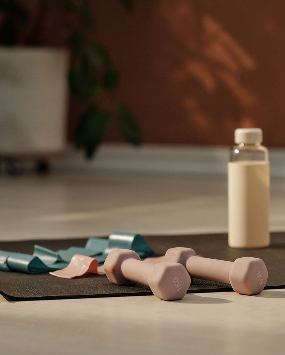 grey mat with group of dumbbells and bottle of water prepared for home fitness training on the floor of spacious living room of modern apartment