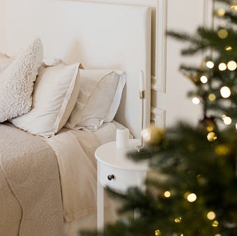 light christmas bedroom with christmas tree bed with beige i white pillows, cushions and blanket near christmas tree