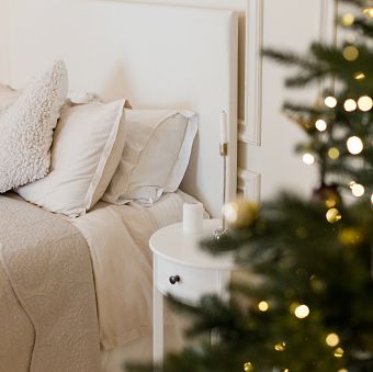 light christmas bedroom with christmas tree bed with beige i white pillows, cushions and blanket near christmas tree