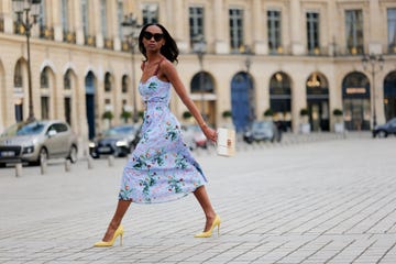 paris, france april 29 emilie joseph wears black large sunglasses, crystal earrings, a pale blue with red green navy blue beige flower print pattern heart neck tank top belted midi dress, gold bracelets, a beige wickers and white shiny leather bi material handbag, yellow shiny leather pointed pumps heels shoes , during a street style fashion photo session, on april 29, 2023 in paris, france photo by edward berthelotgetty images