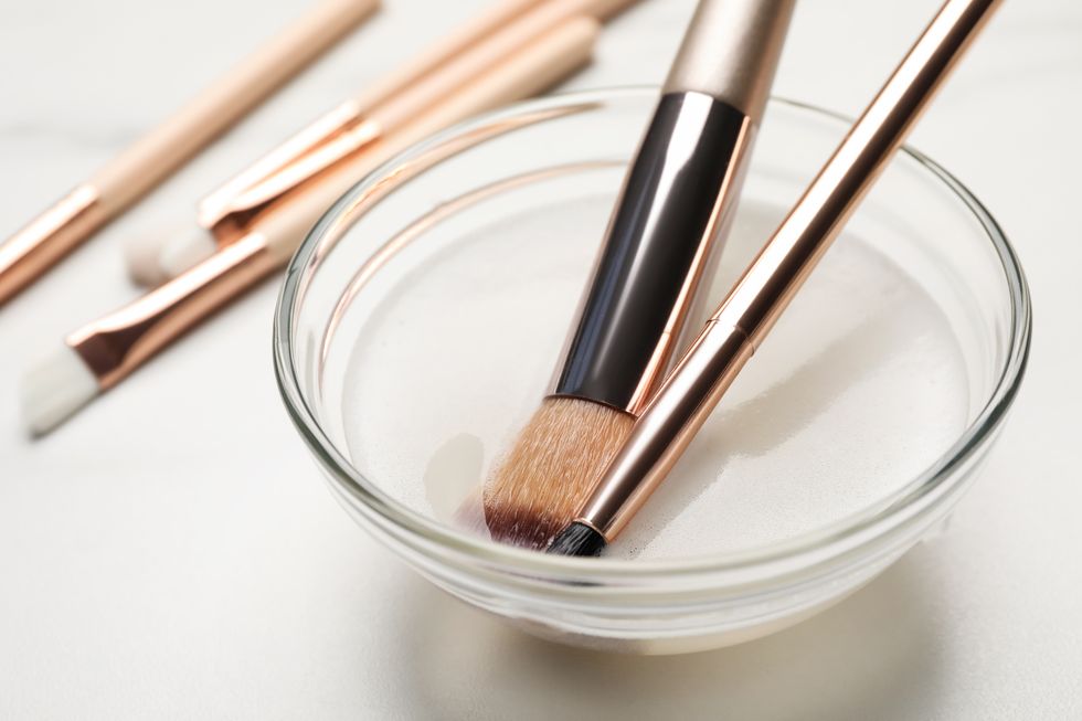 clean makeup brushes in bowl with cleanser on white table, closeup