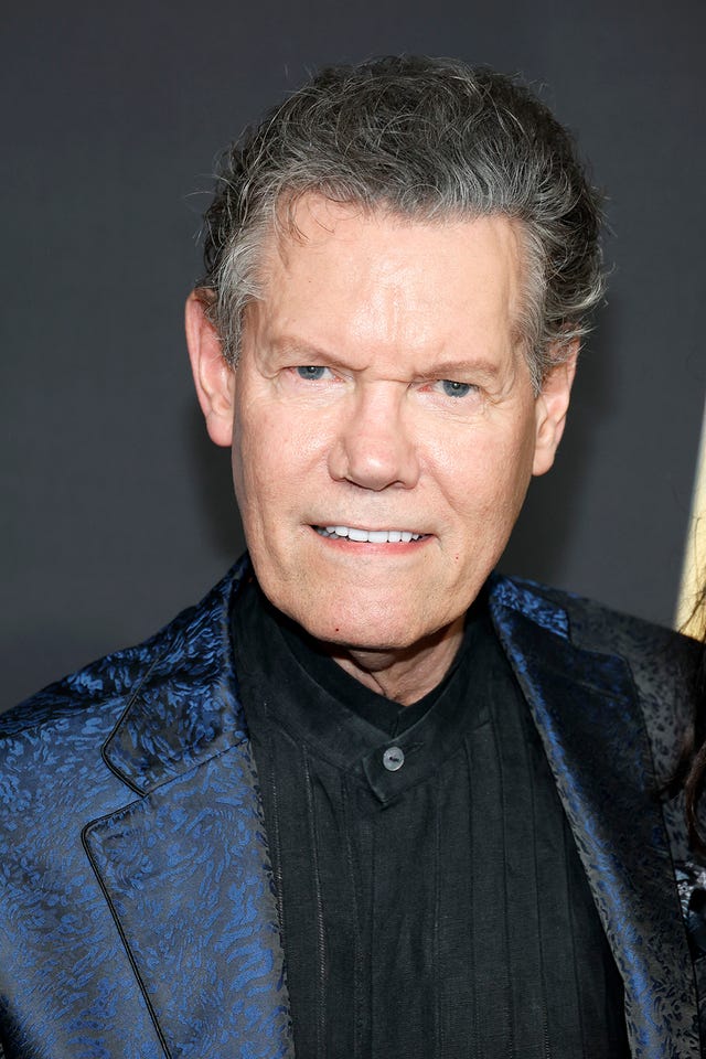 randy travis smiles at the camera, he wears a blue patterned suit jacket and black shirt (photo by jason kempin/getty images)