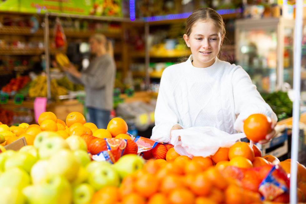 portrait of teenage girl customer buying sweet oranges at grocery shop