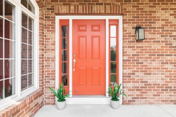 a homes red front door surrounded by red brick and plants sitting in front of the windows