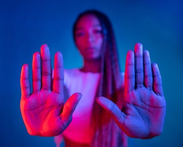 a woman dancing and using her hands with the palms facing the camera for a stop gestures against a blue background focus on foreground