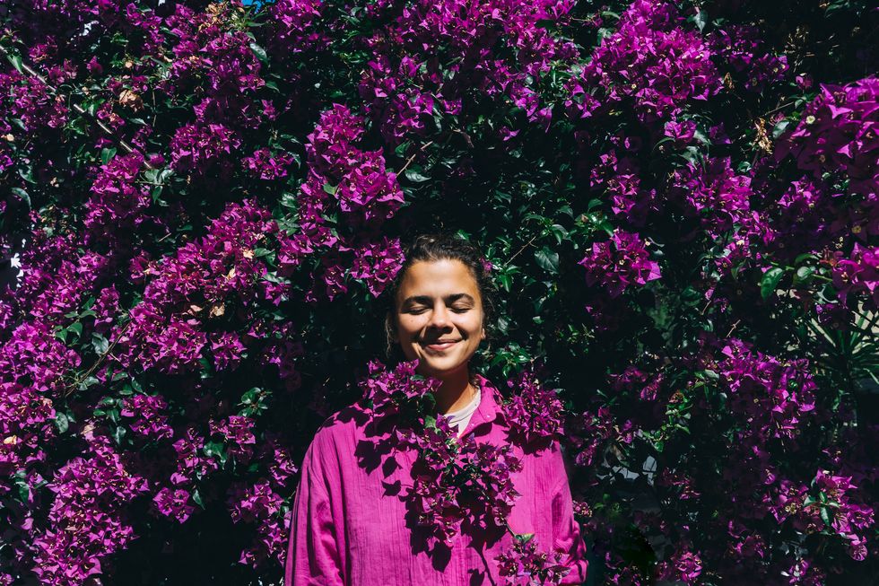 beautiful happy woman in a bright shirt against the background of a bright purple bougainvillea