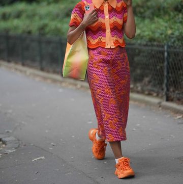 paris, france june 21 a guest wears neon pink sunglasses, pink earrings, a red  orange  pink wavy striped print pattern braided wool short sleeves  shirt neck buttoned polo shirt, a neon pink embossed polka dots print pattern with embroidered orange pattern long tube skirt, a green and orange tie and dye print pattern large shoulder bag, white socks, orange shiny leather sneakers , outside rhude, during the menswear springsummer 2024 as part of paris fashion week on june 21, 2023 in paris, france photo by edward berthelotgetty images