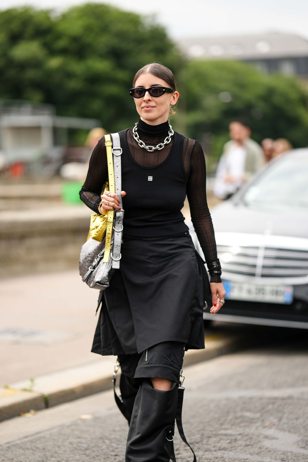 paris, france june 22 a guest wears black sunglasses, a silver large chain necklace, a black tulle long sleeves turtleneck t shirt, a black ribbed tank top, a silver and gold shiny varnished leather large shoulder bag, a black knees skirt, black cut out belted large pants, black shiny leather platform soles heels shoes , silver rings , outside givenchy, during the menswear springsummer 2024 as part of paris fashion week on june 22, 2023 in paris, france photo by edward berthelotgetty images