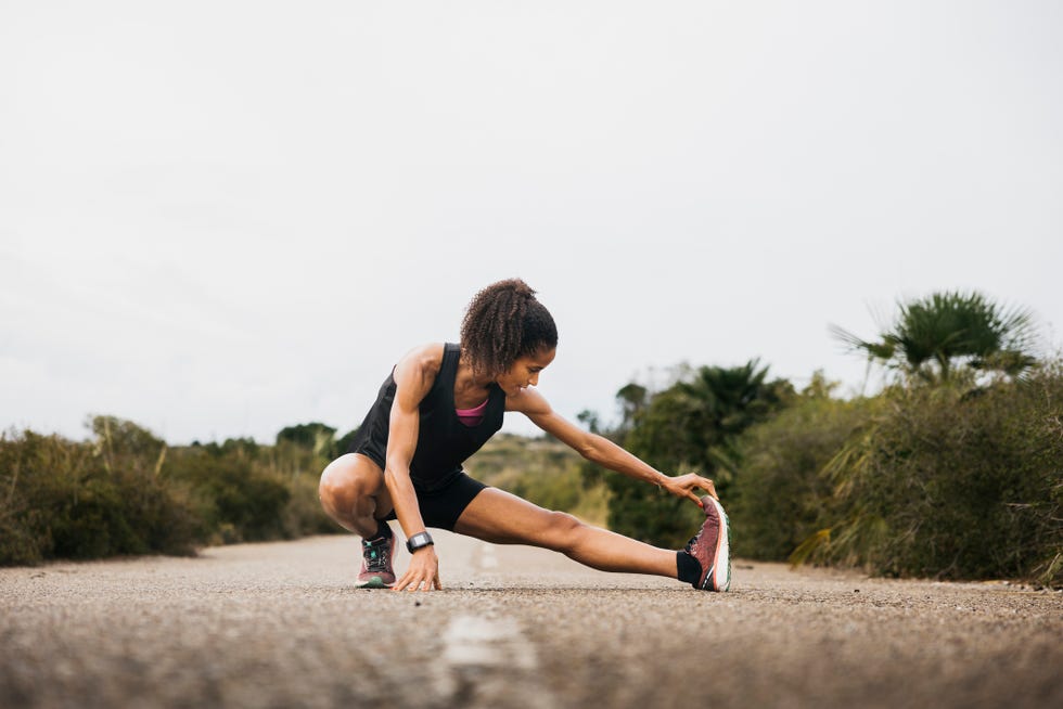 female runner stretching on an empty road woman with fit body warming up on an empty road