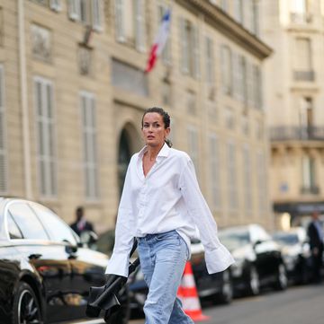 paris, france july 02 a guest wears a white oversized shirt, pale blue faded denim large pants, a black shiny leather chair from alaia, black shiny leather strappy heels sandals , outside alaia, on july 02, 2023 in paris, france photo by edward berthelotgetty images