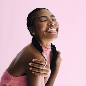 beautiful young black woman embracing herself, shot in front of a pink backdground stock photo