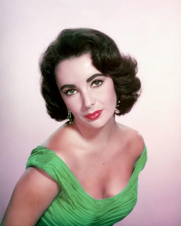 a woman subtly smiles at the camera, she wears dangling earrings and a green off the shoulder dress