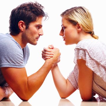 side view of an attractive young couple arm wrestling against white background
