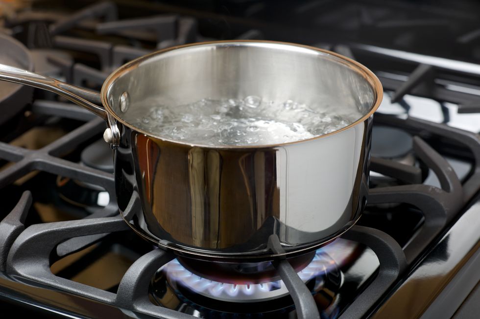 water bubbles and boils on a gas stove or range in a home kitchen blue flame and stainless steel pot