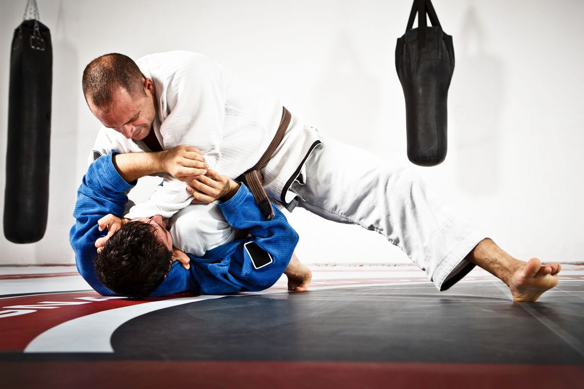 Two individuals grappling on a mat in jiu-jitsu uniforms.