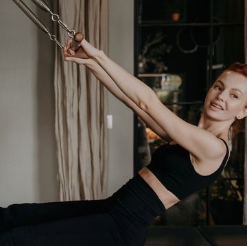 redhead woman does arm stretching on pilates reformer in studio smiling, enhancing muscle strength embracing healthy lifestyle and fitness