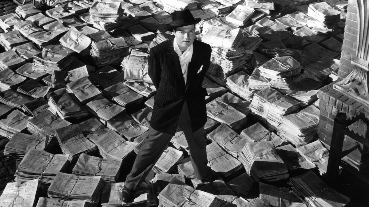 Orson Welles standing on stacks of newspapers in a scene from the film 'Citizen Kane'