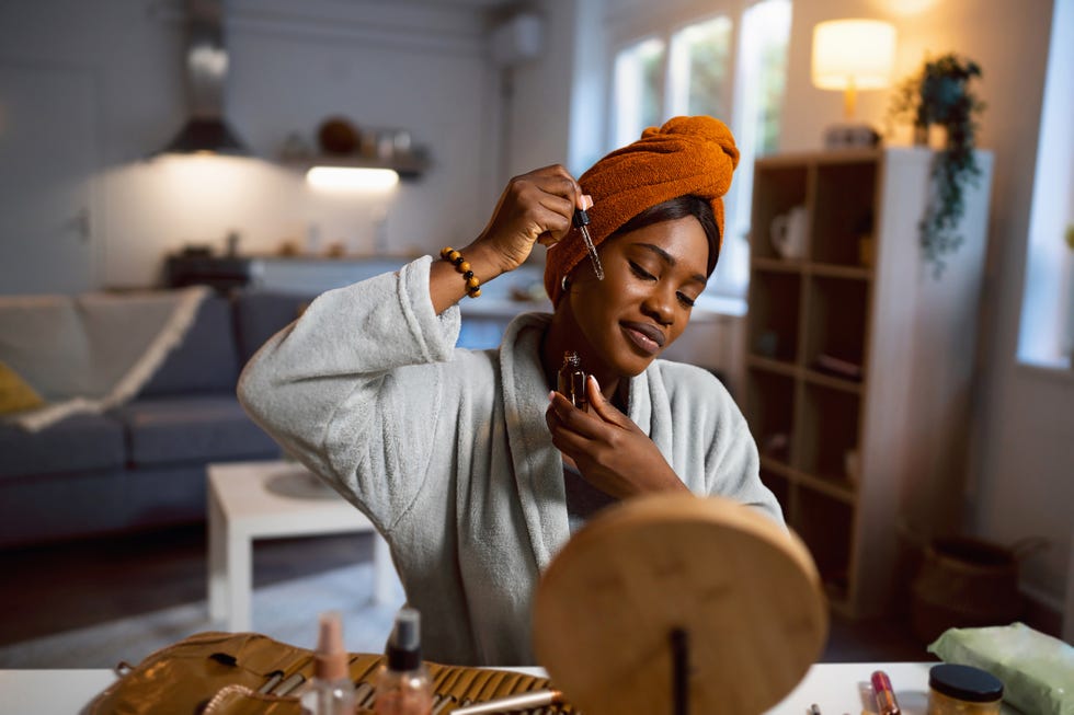 young woman of black ethnicity, applying a face serum, while doing a skin care routine