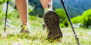 woman hiking in mountains, adventure and exercising nordic walking in sunny  summer nature outdoors legs and sport shoes walk on grass